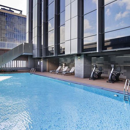 فندق سيزار مترو تايبيه المظهر الخارجي الصورة The photo shows a modern outdoor swimming pool surrounded by a sleek, contemporary building. The pool has a clear blue surface and is bordered by a wooden deck. There are a few lounge chairs placed around the pool for relaxation. In addition, some ex