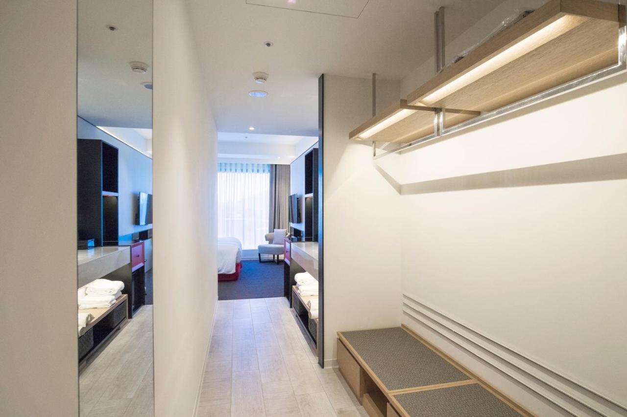 فندق سيزار مترو تايبيه المظهر الخارجي الصورة The photo shows a modern hotel room corridor. On one side, there's a small area with shelving and a bench. The opposite side features dark cabinetry and a large mirror. In the background, light filters in through a window with drapes, revealing a gli