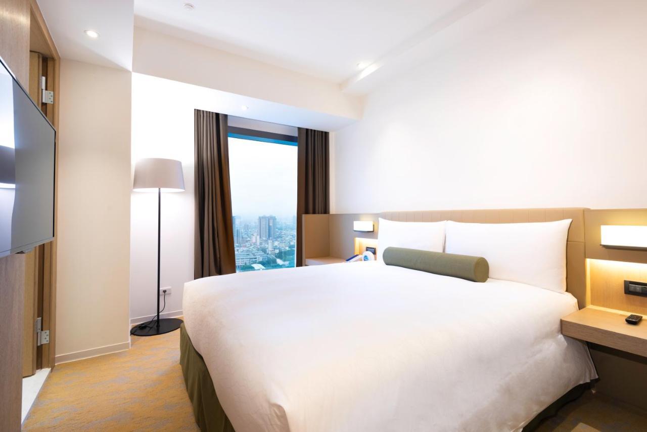 فندق سيزار مترو تايبيه المظهر الخارجي الصورة The photo shows a modern hotel room with a simple and clean design. It features a double bed with white bedding and a green accent pillow. There are two large windows with dark curtains, allowing natural light to enter. A floor lamp stands beside the