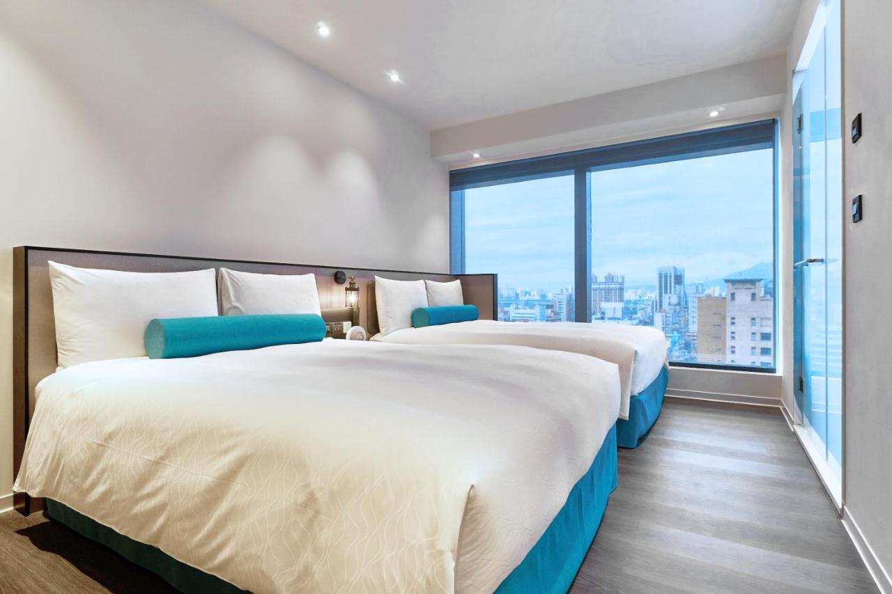 فندق سيزار مترو تايبيه المظهر الخارجي الصورة The photo depicts a modern hotel room featuring two beds. The beds have white bedding and turquoise accent pillows. Large windows allow natural light to enter, providing a view of the city outside. The room has a contemporary design, with a clean and