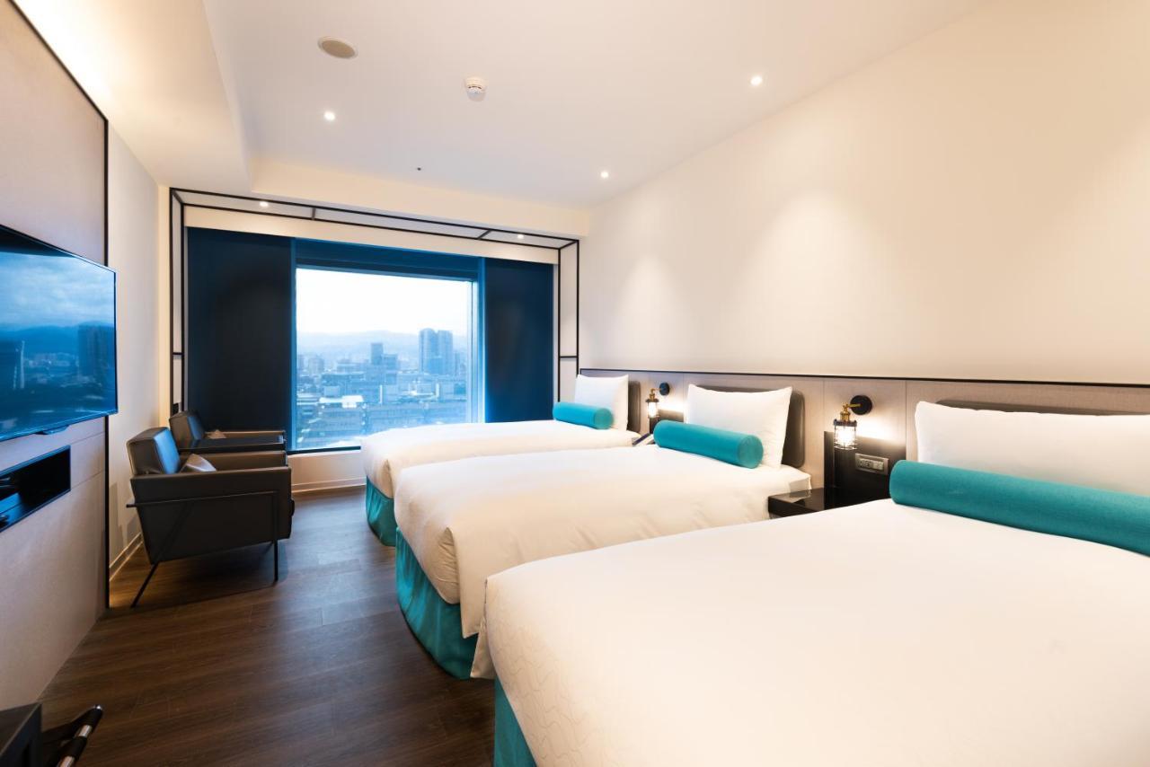 فندق سيزار مترو تايبيه المظهر الخارجي الصورة The photo shows a modern hotel room featuring two beds with white bedding and light blue accents. The room has sleek, contemporary design elements, including a wall-mounted television and a large window that offers a view of the outside, likely a cit