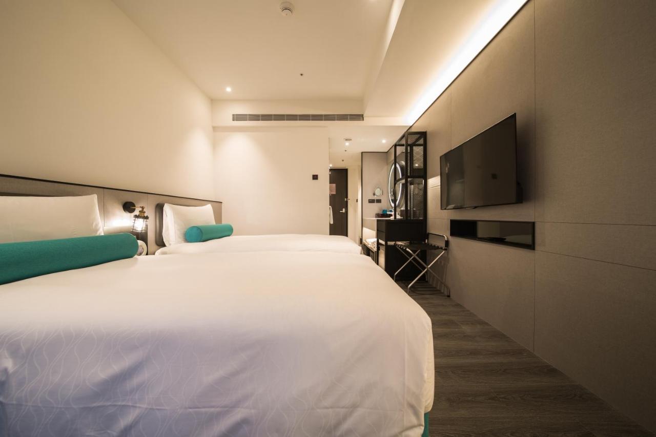 فندق سيزار مترو تايبيه المظهر الخارجي الصورة The photo shows a modern hotel room featuring two beds with white linens and teal accents. The walls are a light, neutral color, contributing to a clean and contemporary aesthetic. There is a minimalist design, with a mounted flat-screen TV on one wa